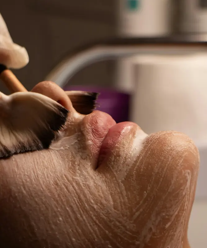 Pincel aplicando máscara cremosa no rosto durante um tratamento facial